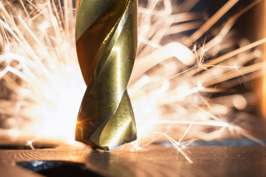 Närbild på en metallborr som borrar i metall, med gnistor som flyger i bakgrunden. Bilden används för att illustrera skillnaden metallborr vs träborr.