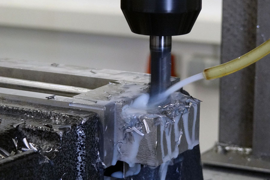 Närbild på en metallborr som borrar i ett uppspänt metallstycke, med kylarvätska riktad mot arbetsområdet. Bilden illustrerar industriell borrning och skillnaden mellan metallborr och träborr.