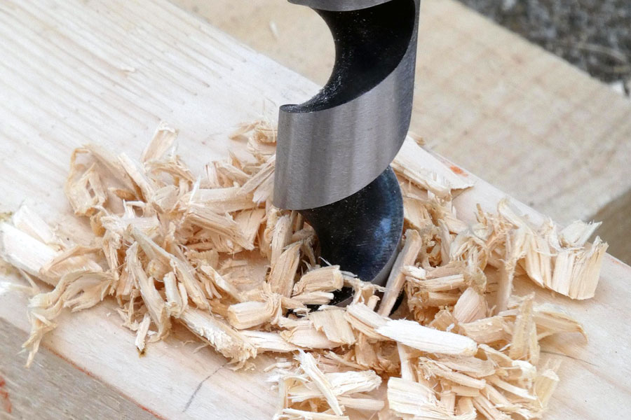 Närbild på en träborr som borrar i träregel, med flis runt hålet. Bilden används för att illustrera skillnaden mellan metallborr vs träborr.
